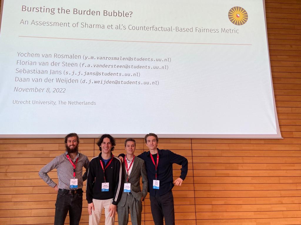 The four authors in front of the title slide at BNAIC 2022